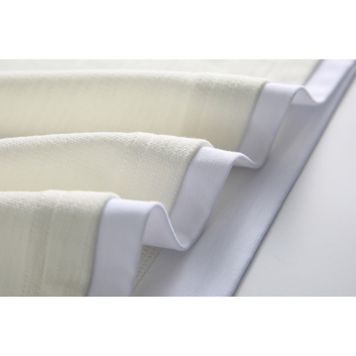 Close-up of layered ivory fabric and white ribbed trim at the shirt hem.