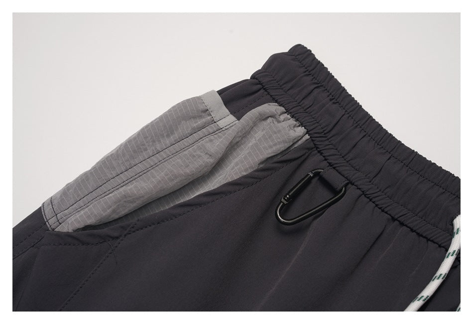 Close-up of a gray side pocket panel, elastic waistband, and black metal clip on charcoal pants.