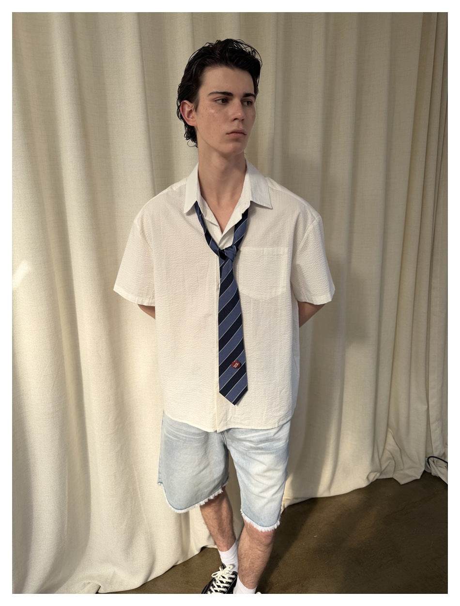 Front view of a model wearing a white short-sleeve shirt with a chest pocket and navy striped tie.