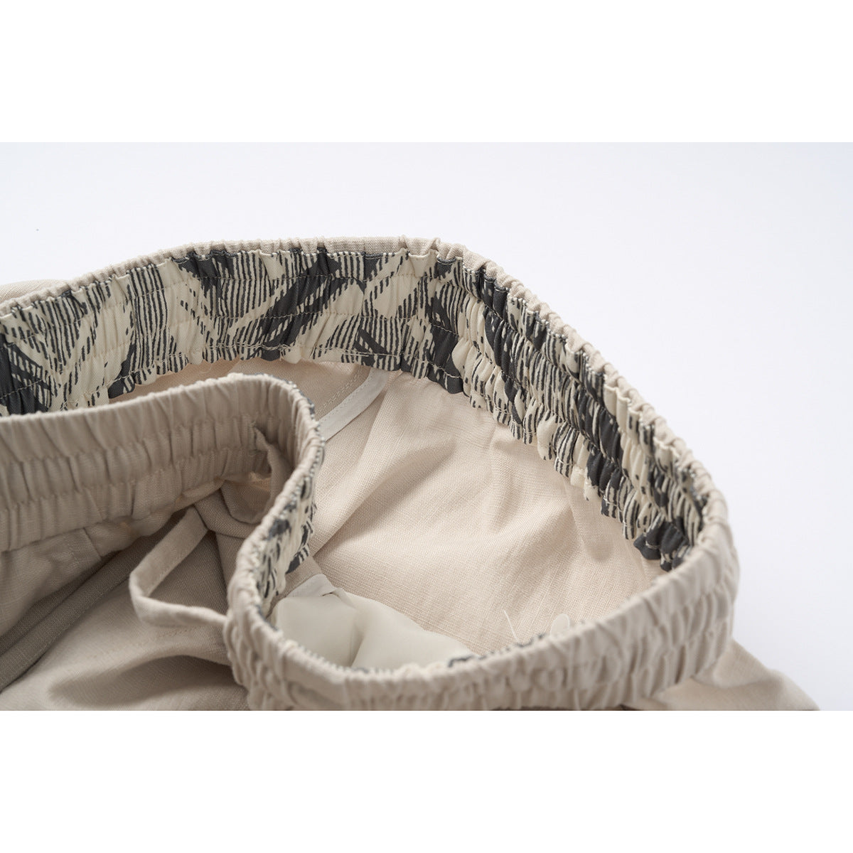 Inside view of light beige shorts with a black-and-cream patterned lining along the gathered waistband.
