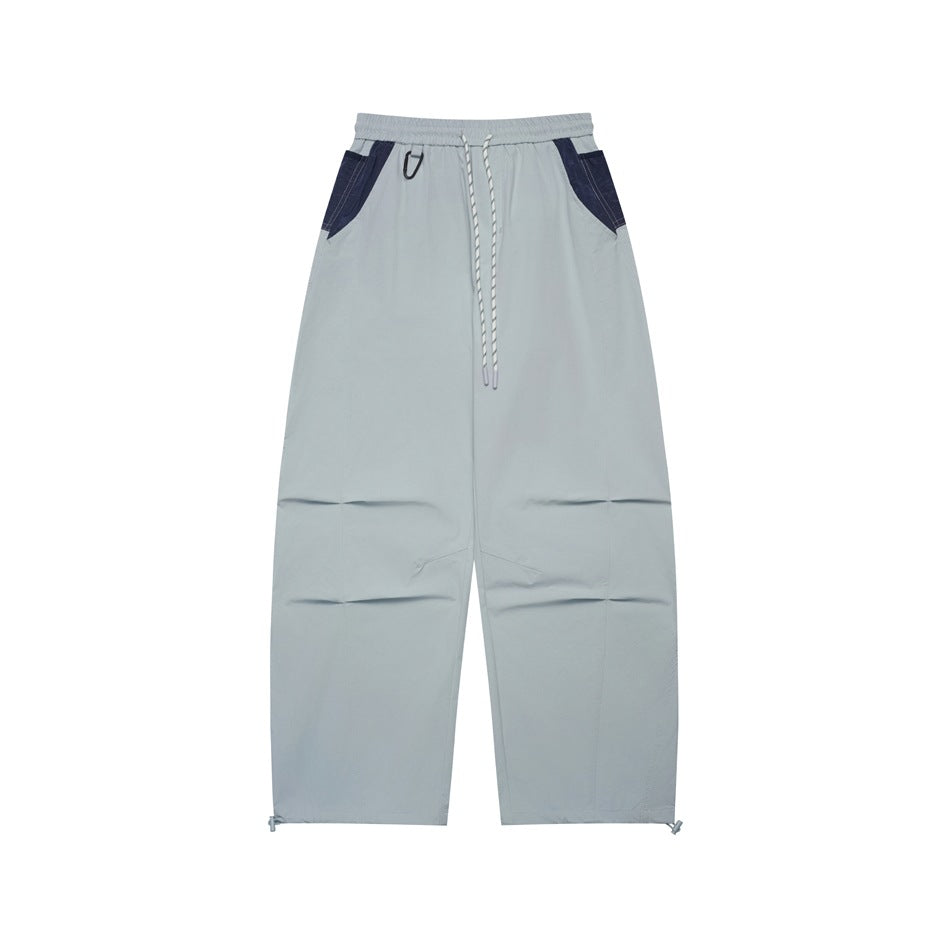 Light gray-blue wide-leg drawstring pants with navy pocket panels and knee pleats, flat front view