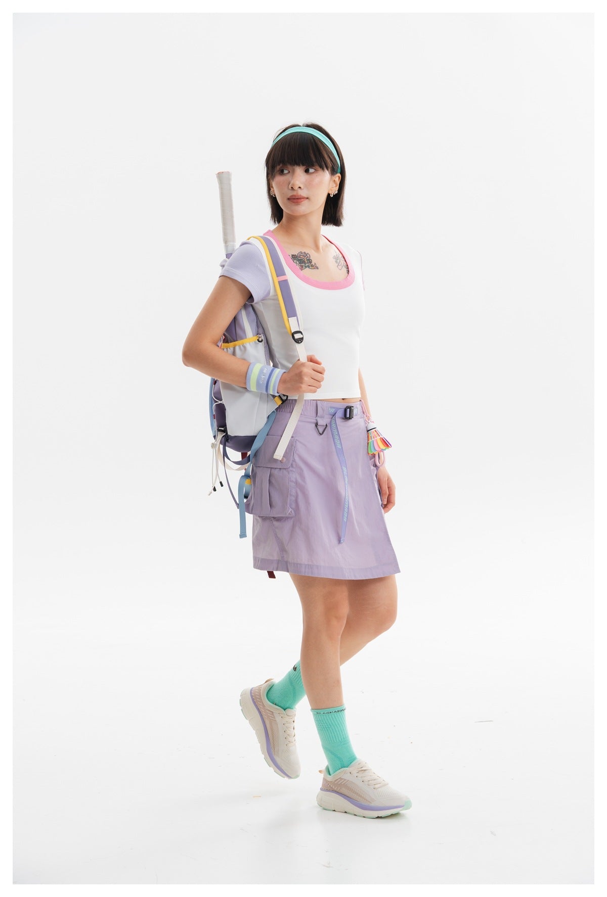 Model in a white crop top with pink neckline and lilac sleeves, paired with a lavender cargo skirt and backpack.