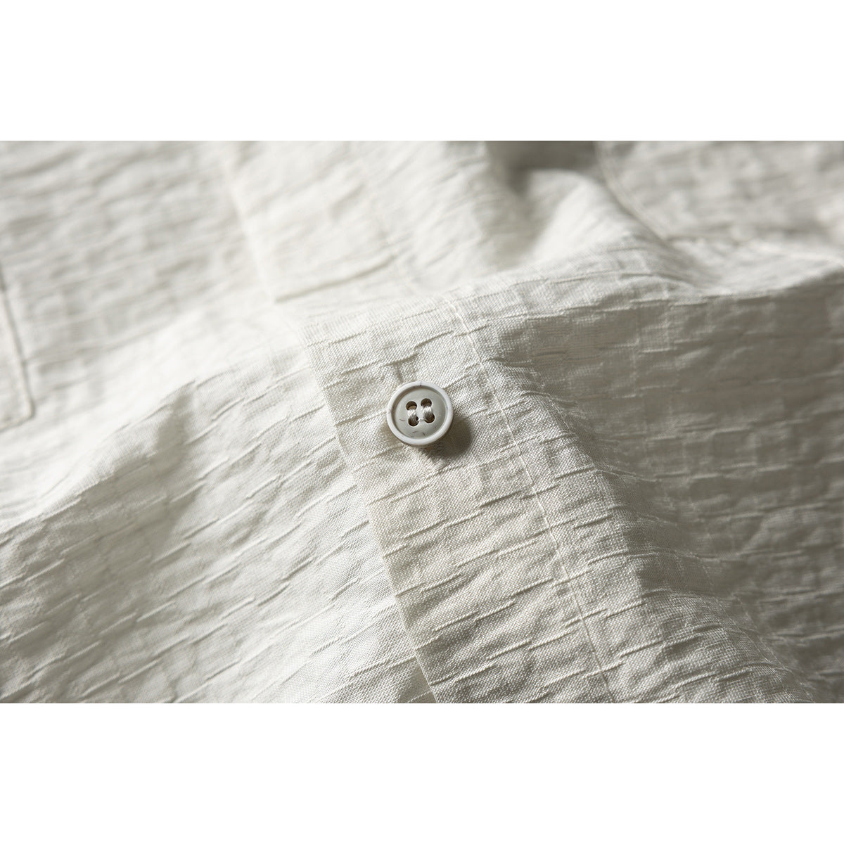 Close-up of a light button and stitched placket on textured off-white shirt fabric.