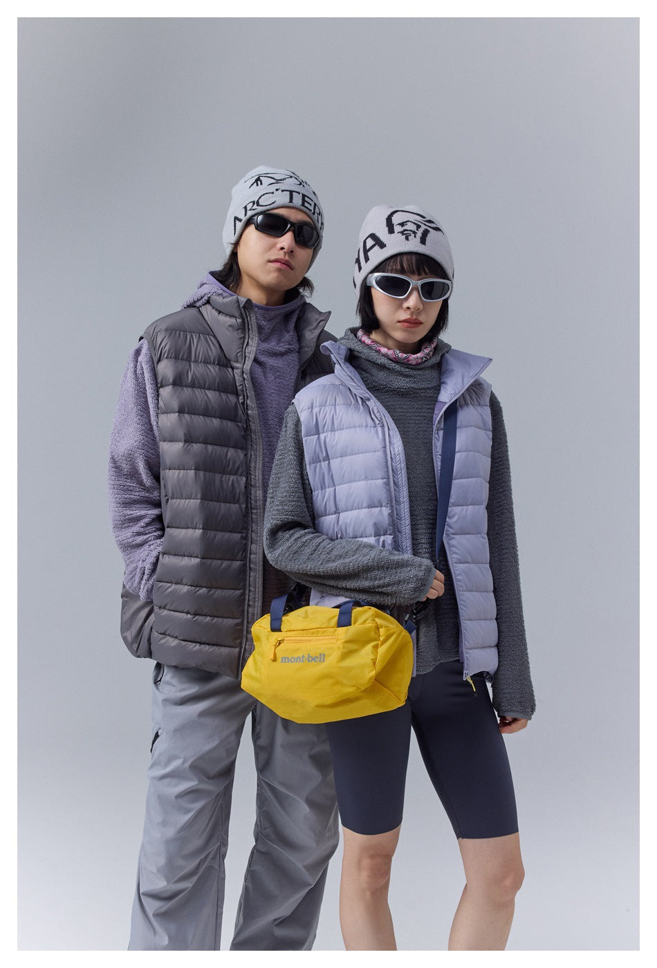 Two models pose in charcoal and pale lavender quilted vests; a yellow bag is held in front.