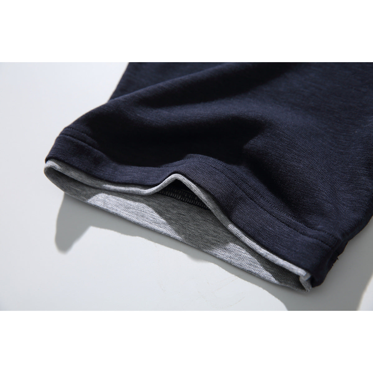Close-up of a navy T-shirt hem folded to show the light gray inner layer and stitching.