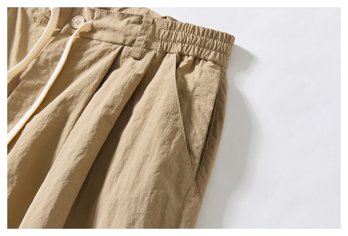 Close-up of beige trousers showing the gathered waistband, button, belt loop, pleats, and side pocket.
