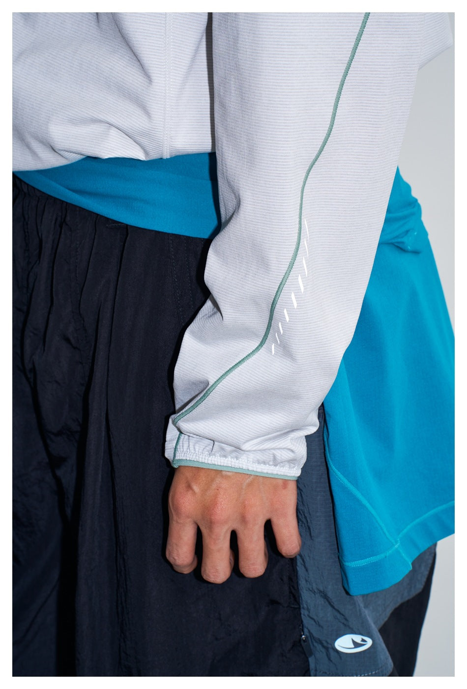 Close-up of the pullover's white sleeve with teal piping and elastic cuff beside black pants and a turquoise layer.