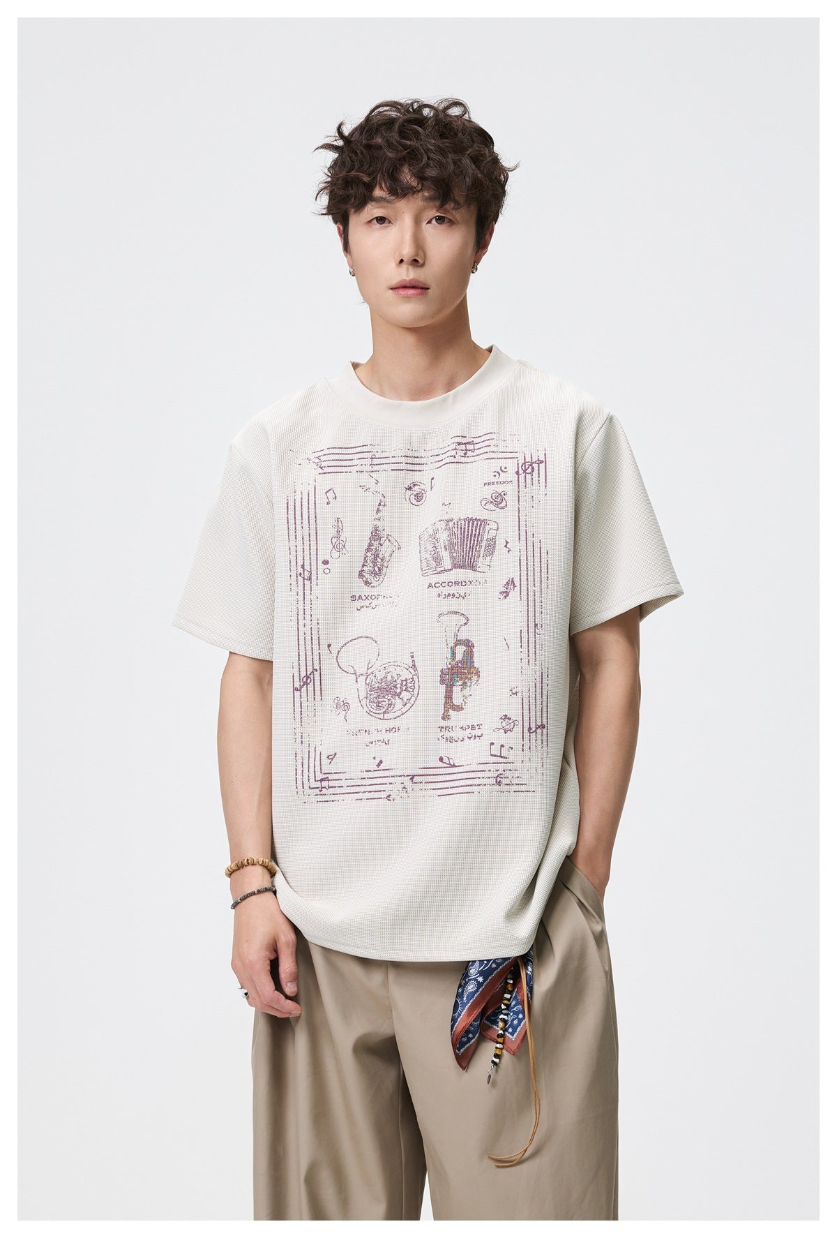 Front view of a model wearing an ivory short-sleeve T-shirt with a burgundy musical-instrument print.