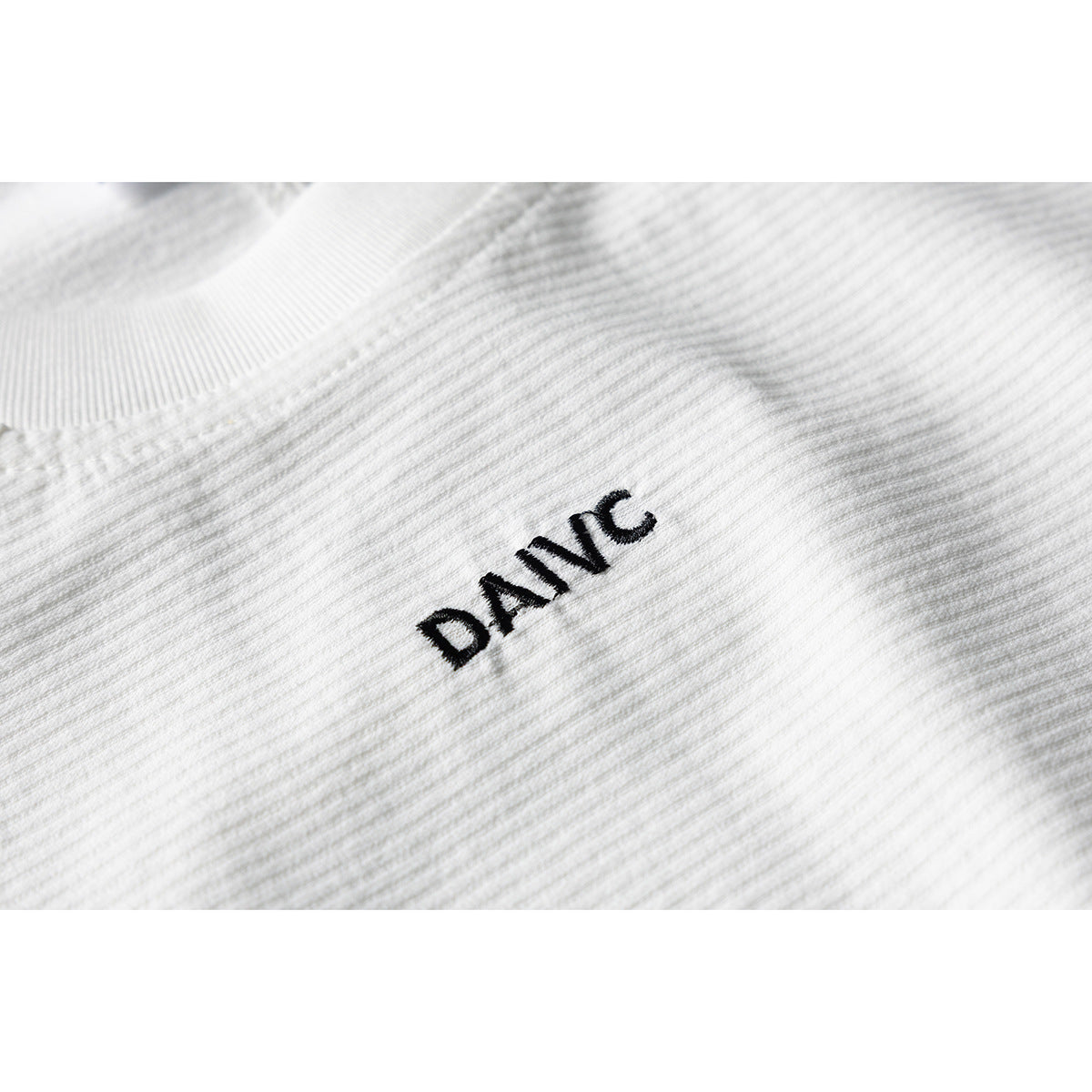 Close-up of black embroidered lettering on the textured white shirt fabric.