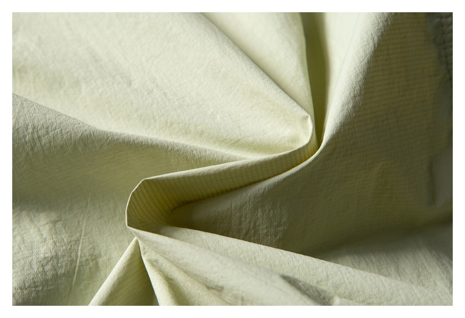 Close-up of pale sage fabric folded to show its textured surface and fine grid-patterned inner layer.