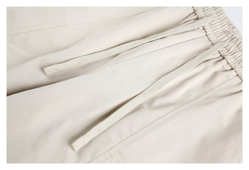 Close-up of light beige pants with two drawstrings emerging from an elastic waistband.