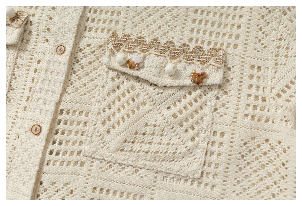 Close-up of an ivory openwork shirt’s chest pocket with decorative trim and ornamental buttons.