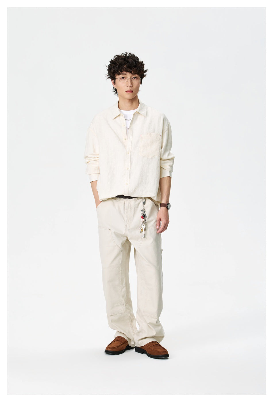 Man standing in a cream oversized button-up shirt with chest pocket, cream pants and brown loafers