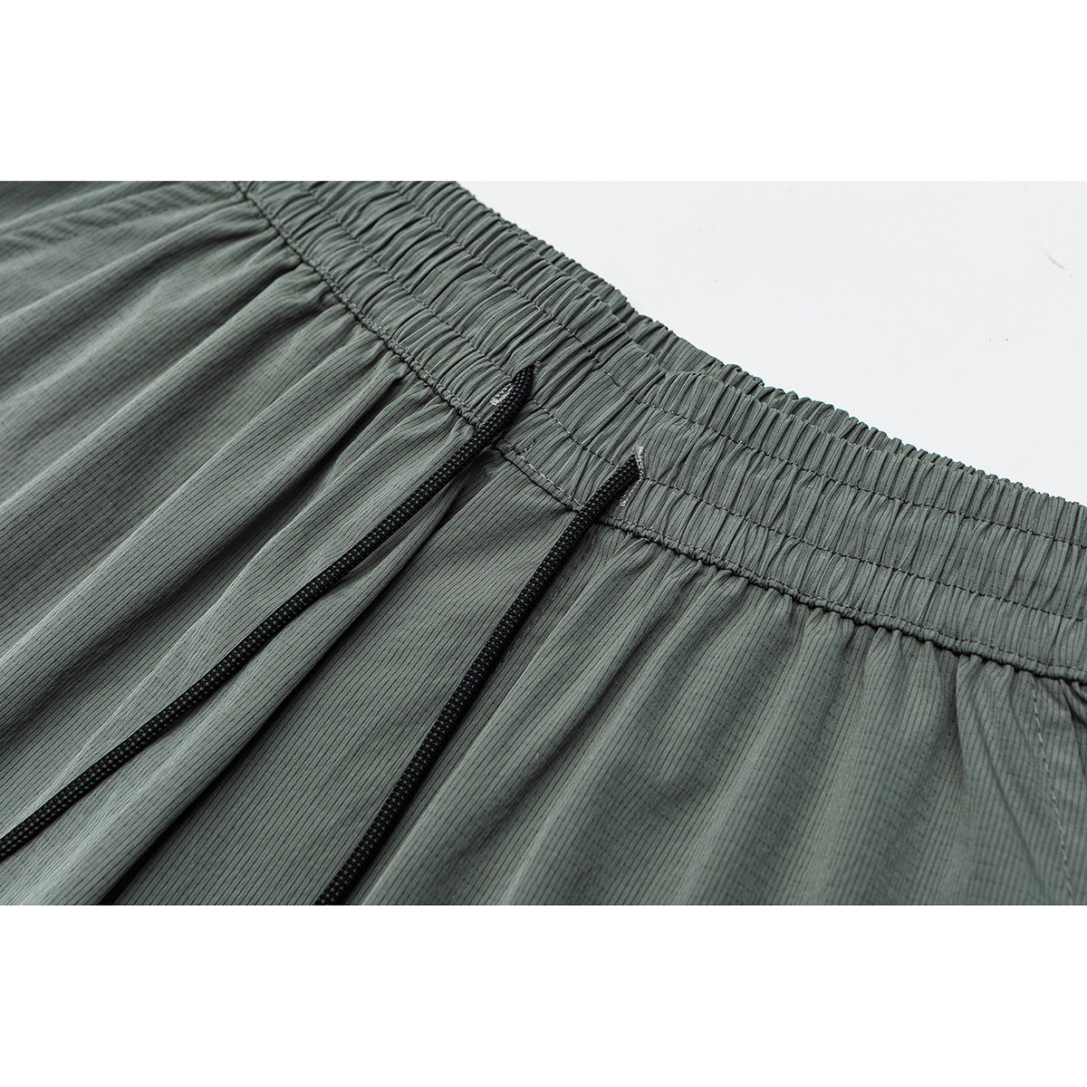 Close-up of gray-green striped shorts with a gathered elastic waistband and black drawstrings.