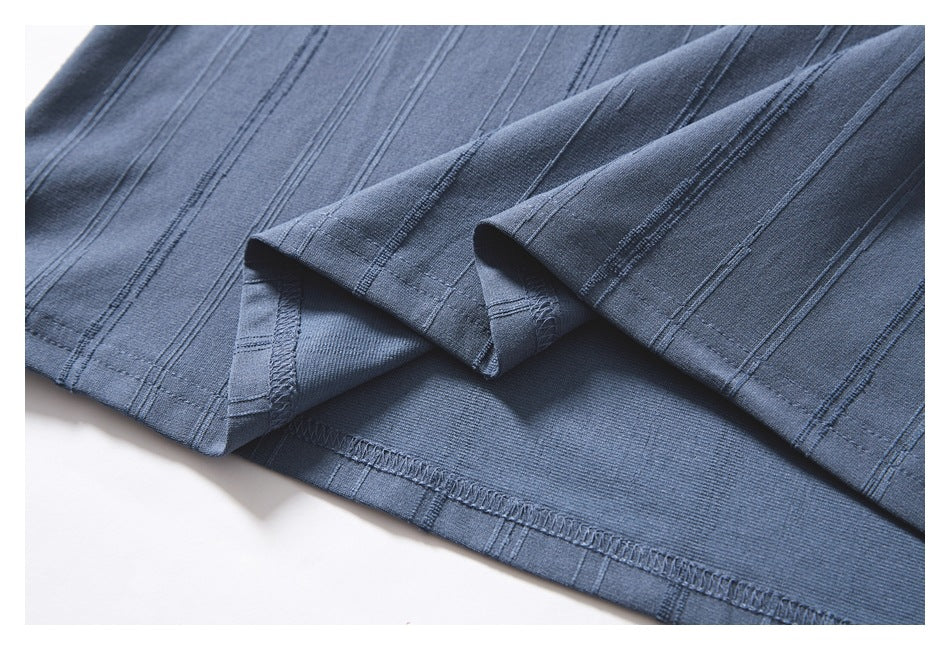 Close-up of blue-gray fabric with parallel stitched lines and a folded, overlocked hem.