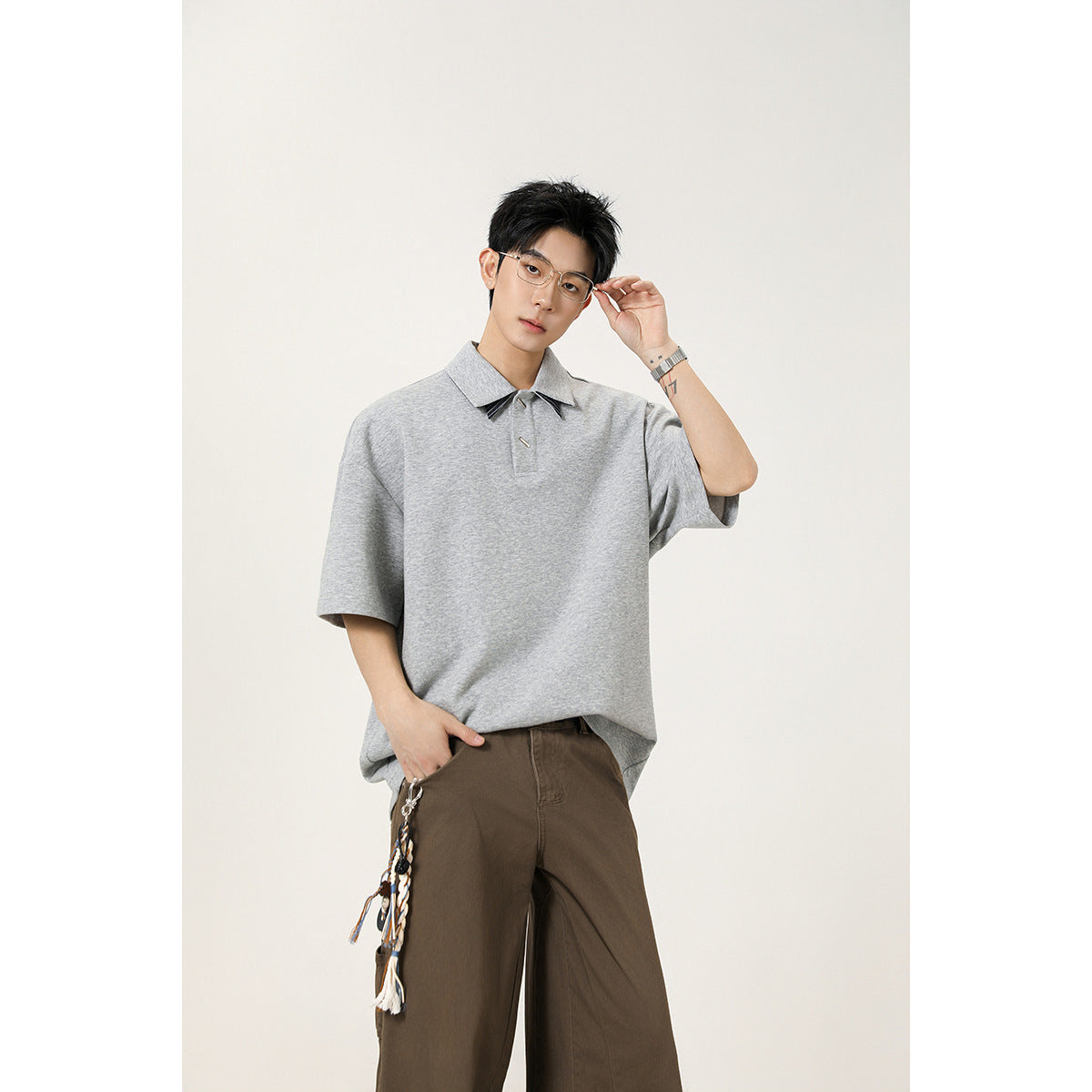Model wearing a heather-gray oversized short-sleeve polo with pointed collar and decorative accents, shown from the waist up.