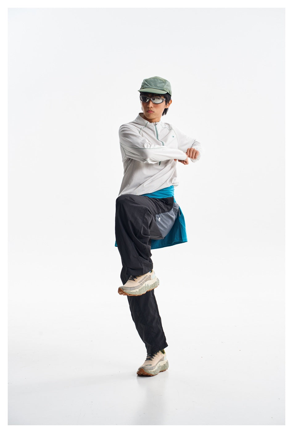 Model posing in a white zip-neck pullover, loose black pants, and a turquoise layer tied at the waist.