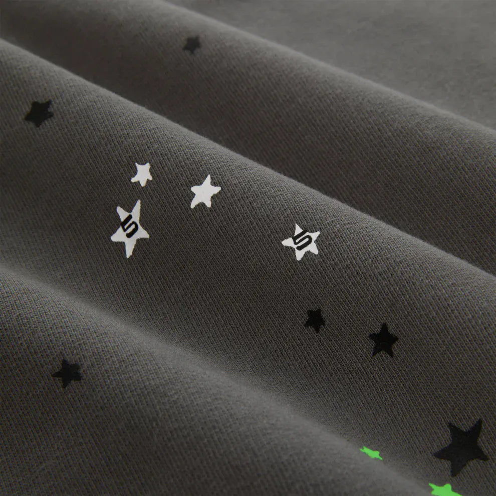 Close-up of olive green fabric from the Sp5der “P!nk! Hares the Slime” Hoodie – a 440GSM heavyweight spider-web pullover with small black, white, and green stars—some featuring a stylized S—for a streetwear look.