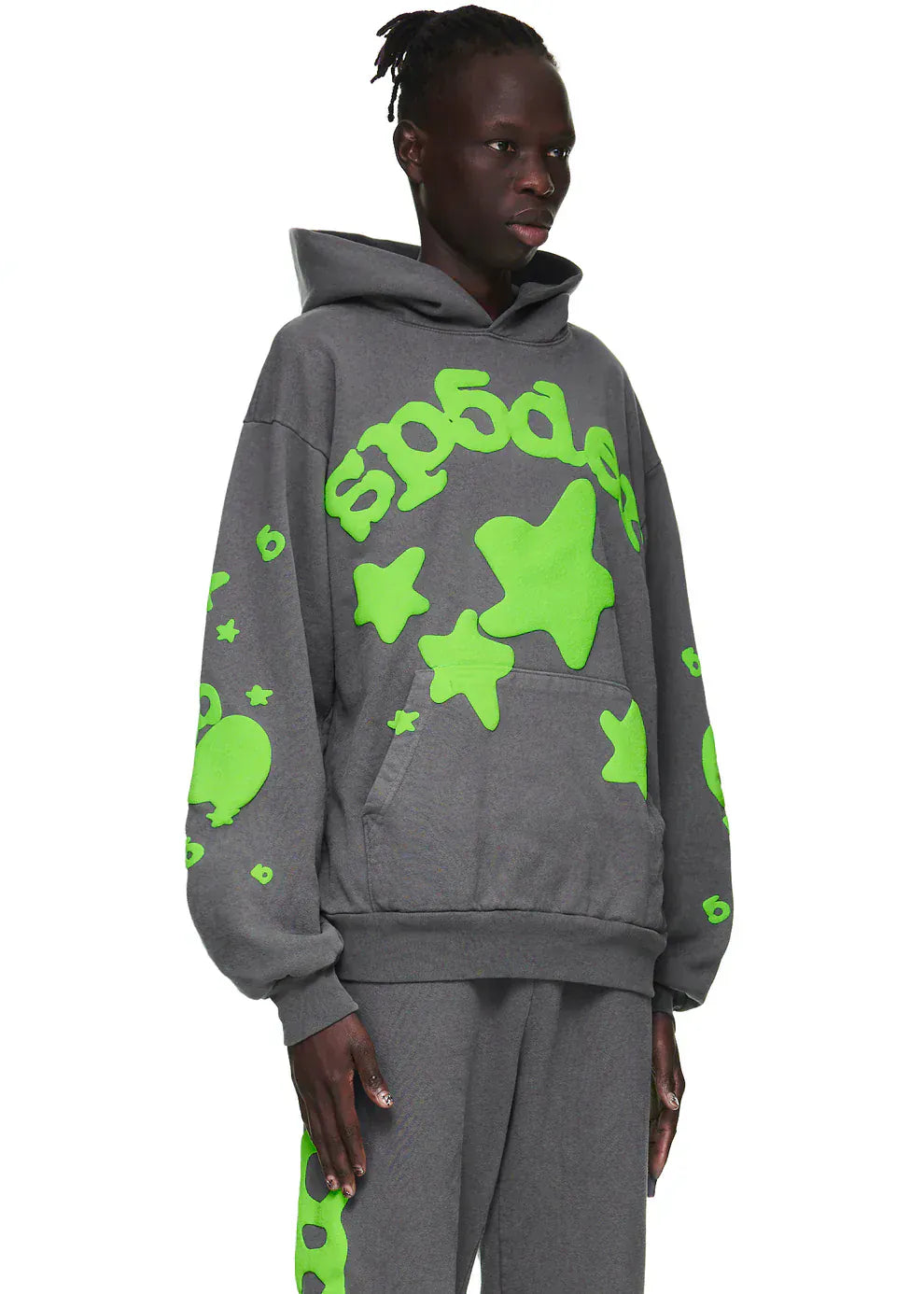 A person wears the Sp5der 440GSM Heavyweight Hoodie in grey with neon green star graphics—an oversized, fleece streetwear sweatshirt—styled against a white background.