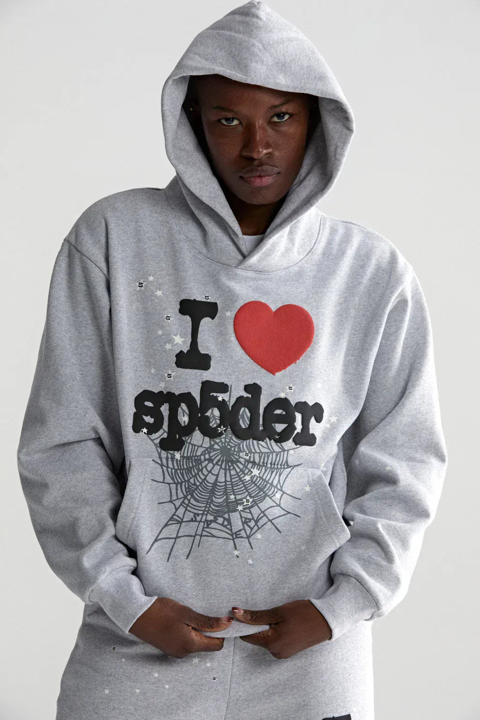 Model wearing the Sp5der “I Love Sp5der” Hoodie – Grey 440GSM Heavyweight Oversized Pullover with red heart and spiderweb graphics, "sp5der" text, and a Y2K streetwear vibe, styled against a plain background.