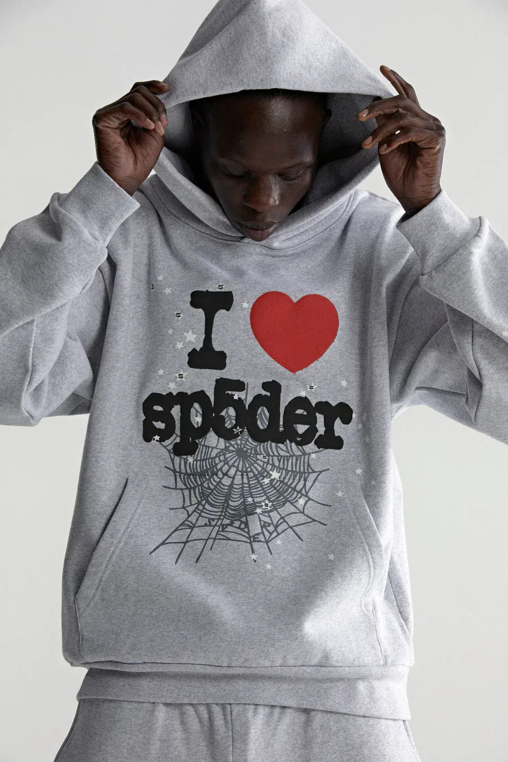 Someone wears the Sp5der “I Love Sp5der” Hoodie – Grey 440GSM Heavyweight Oversized Streetwear Pullover, with “I ♥ spider” and a web graphic, pulling the hood over their head.