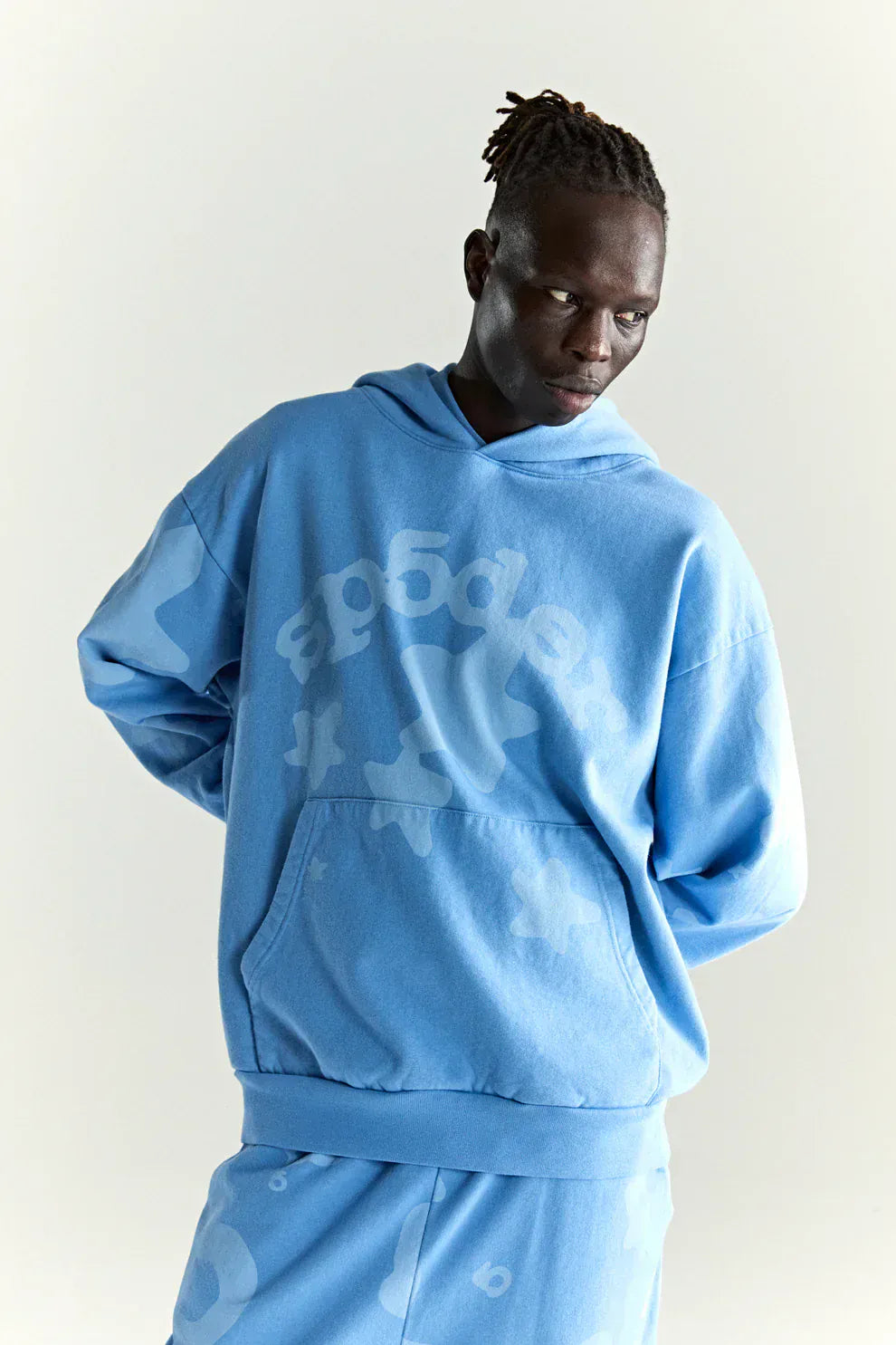 A person in a baby blue Sp5der Star Hoodie – 440GSM heavyweight oversized streetwear pullover with abstract patterns and "sp5der" on the front perfectly embodies Y2K fashion.
