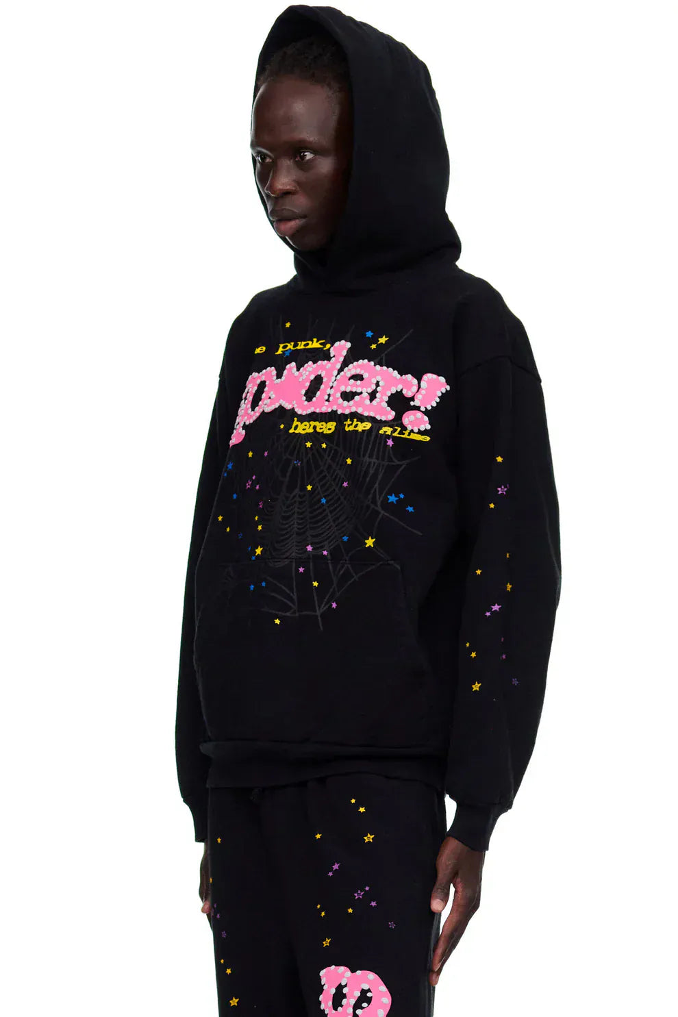 Someone is wearing the Sp5der “Hares the Slime” Hoodie – a black 440GSM heavyweight pullover with colorful graphic text, star and spider-web designs – paired with matching black pants.
