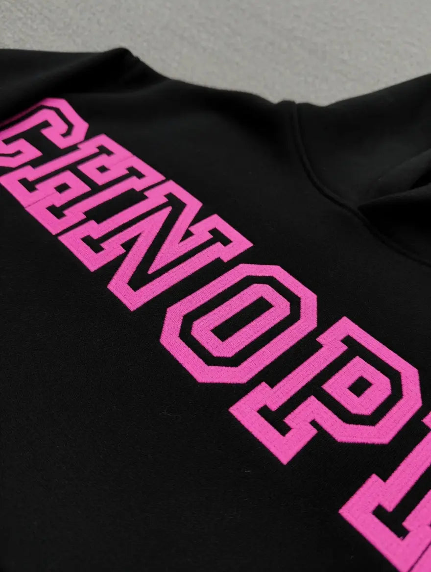 Close-up of the Sp5der Arachnophobia Black Hoodie with bold pink varsity-style lettering across the chest―a must-have streetwear piece.