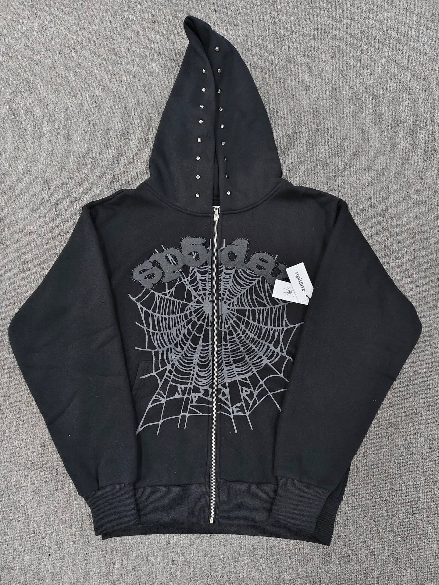 Black Sp5der zip-up hoodie with tonal spiderweb graphic and rhinestone stud hood detailing laid flat