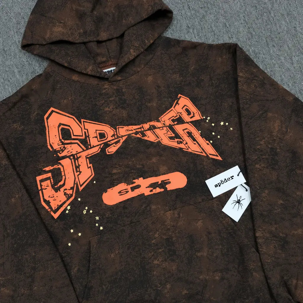 The Sp5der Brown Tie-Dye Hoodie with Orange Logo Print features a bold orange SP5DER logo, skateboard graphic, star accents, and mottled texture. Two tags show "sp5der" and a spider illustration―perfect for standout streetwear style.