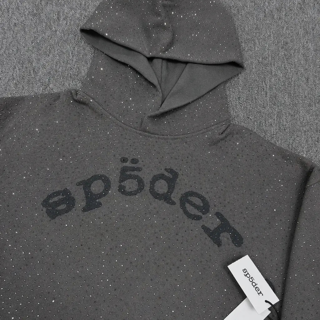 A streetwear staple, the Sp5der Dark Grey Rhinestone Arch Logo Hoodie features sparkly embellishments and a black "sp5der" logo on the chest, with a branded tag on its textured dark grey surface.