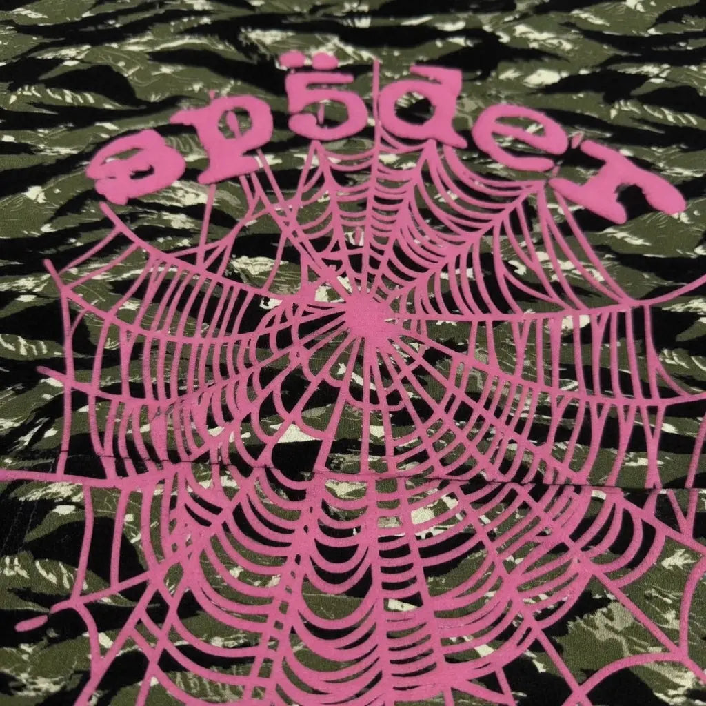 The Sp5der Tiger Camo Hoodie with Pink Spiderweb Logo features a bold pink spiderweb graphic and "Sp5der" text printed on green tiger camo fabric for a standout streetwear look.