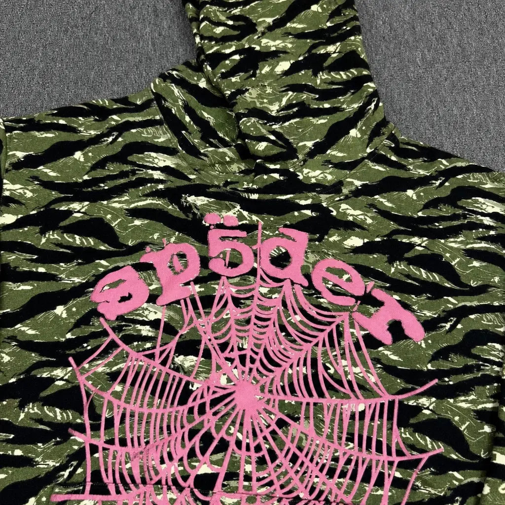 The Sp5der Tiger Camo Hoodie with Pink Spiderweb Logo showcases a green tiger camo and black design, bold pink spiderweb graphic, and distorted pink "sp5der" text―making it a standout piece for any streetwear collection.