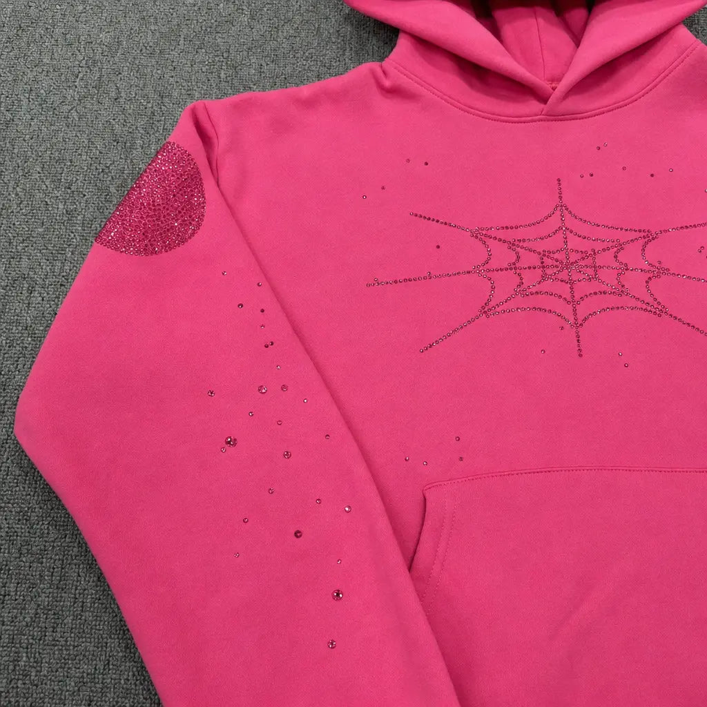 The Sp5der Pink Rhinestone Spiderweb Crystal Hoodie features a hot pink design with rhinestone spiderwebs on the chest, sleeve accents, and a glittery elbow patch―making it the ultimate statement streetwear pullover.