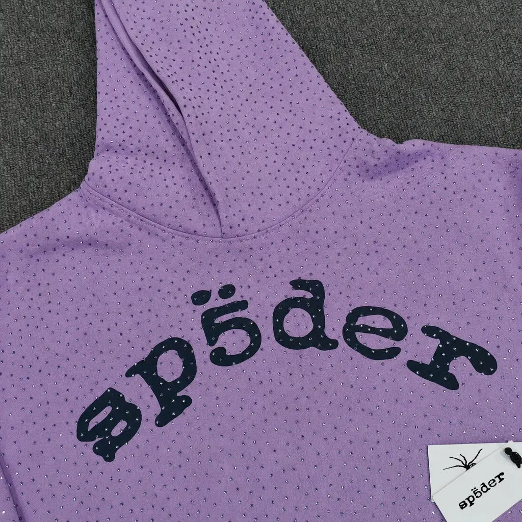The Sp5der Lavender Purple Rhinestone Arch Logo Hoodie features bold black "sp5der" lettering on the front with small rhinestones and comes with a white tag displaying a spider illustration and matching "sp5der" text.