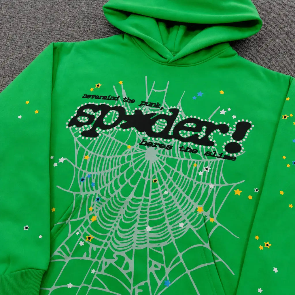 The Sp5der Neon Green Spiderweb Graphic Pullover Hoodie features a bold spiderweb design, colorful stars, and black "spider!" and "reversing the punk" text, shown laid flat on a gray surface.