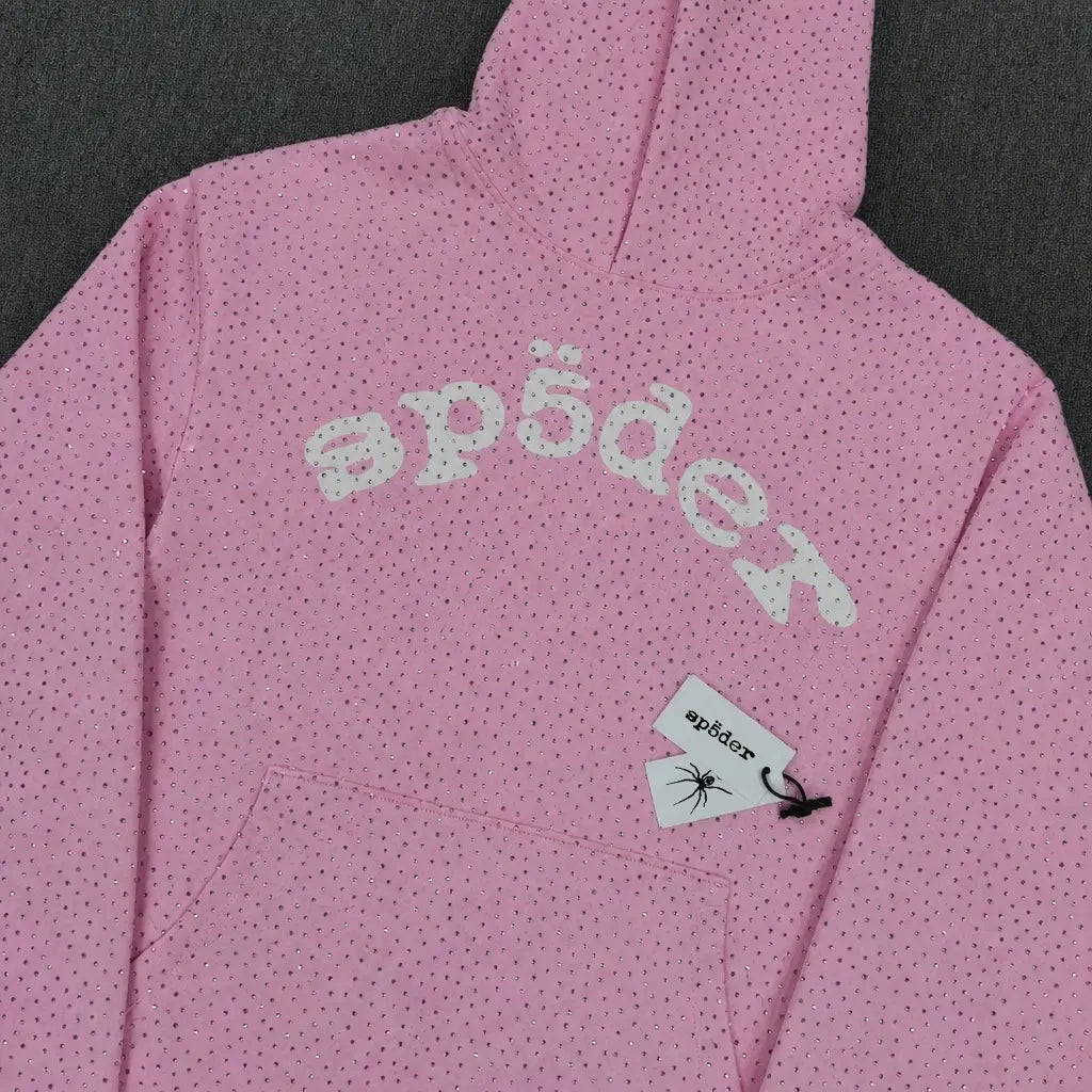 The Sp5der Pink Rhinestone All-Over Arch Logo Hoodie is a pink streetwear piece with black dots, "sp5der" in white across the chest, and a logo tag with a spider graphic near the pocket for standout style.