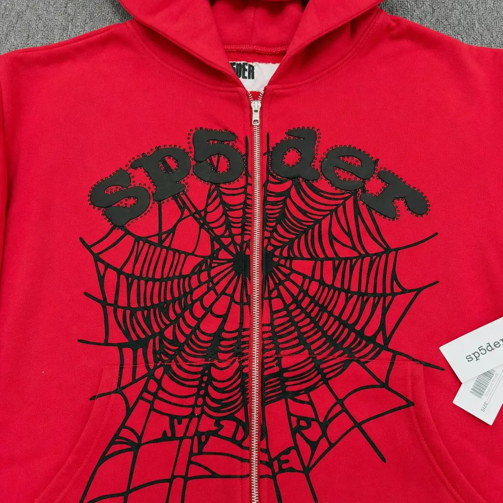 The Sp5der Red Zip-Up Hoodie Black Spiderweb Studded Logo features a bold black spiderweb and "sp5der" lettering on the front, plus a signature white tag on the zipper―making it a standout streetwear essential.