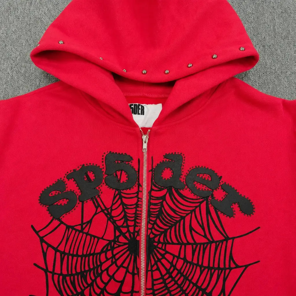 The Sp5der Red Zip-Up Hoodie Black Spiderweb Studded Logo features a bold black spiderweb design, studded hood, and prominent "sp5der" text across the chest, all displayed on a vibrant red streetwear hoodie.