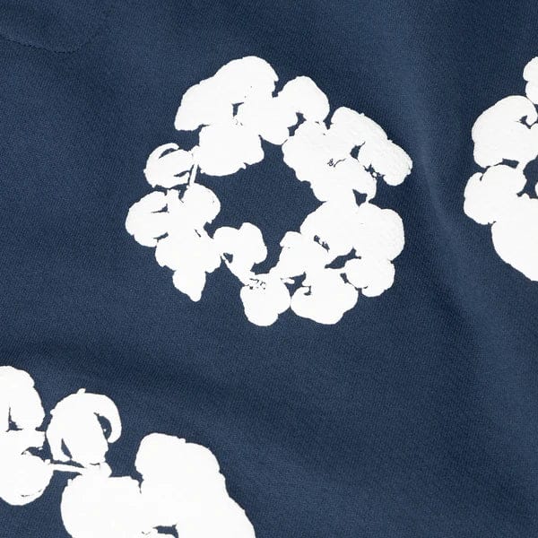 Navy Blue “Cotton Wreath” Denim Tears Sweatpants feature a white floral print reminiscent of cotton wreath patterns, offering stylish streetwear appeal.
