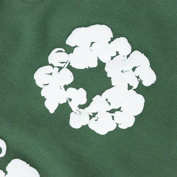 The Forest Green “Cotton Wreath” Denim Tears Sweatpants feature a white floral print inspired by the iconic cotton wreath, creating a bold streetwear look on forest green fabric.
