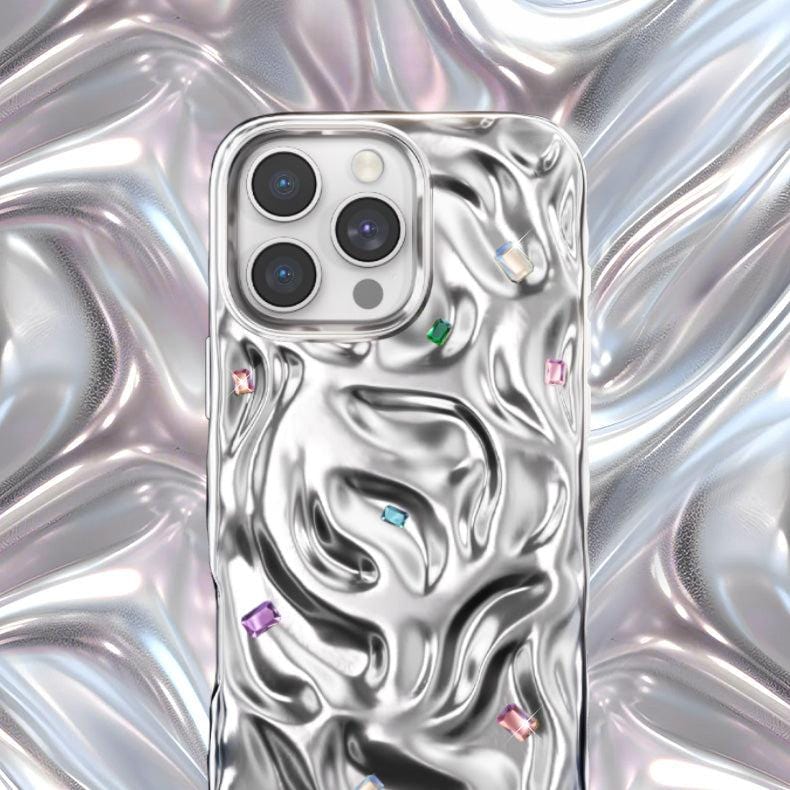 An iPhone 16 Pro Max enclosed in a luxury case crafted from PC material, showcasing handcrafted gemstone detailing with a reflective wavy pattern against a silver background.
