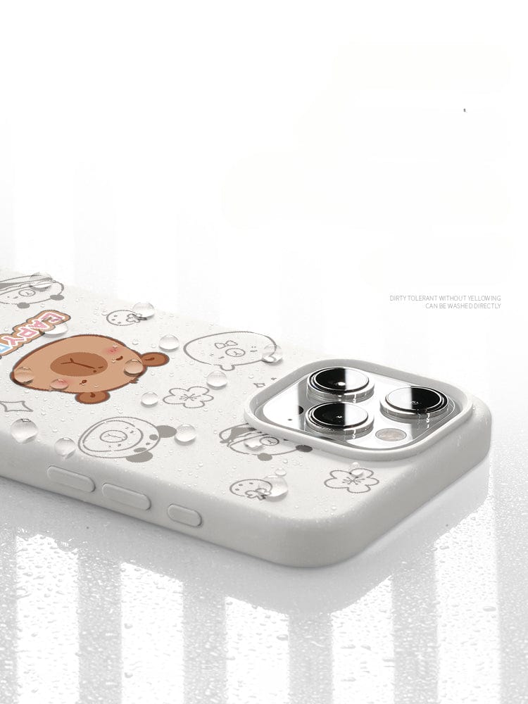 A white iPhone 16 Pro Max case with a cute capybara and floral design, wet with water droplets, lies on a surface. Featuring a triple-layer shockproof structure for all-around protection, it is advertised as dirt tolerant and washable.