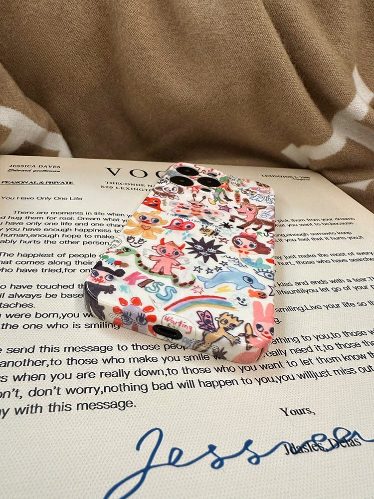 A Whimsical Doodle Art iPhone 16 Pro Max Case, featuring a colorful cartoon design, rests atop a magazine page filled with text and signatures. The beige fabric background, accented by white patterns, adds a subtle elegance to the scene.