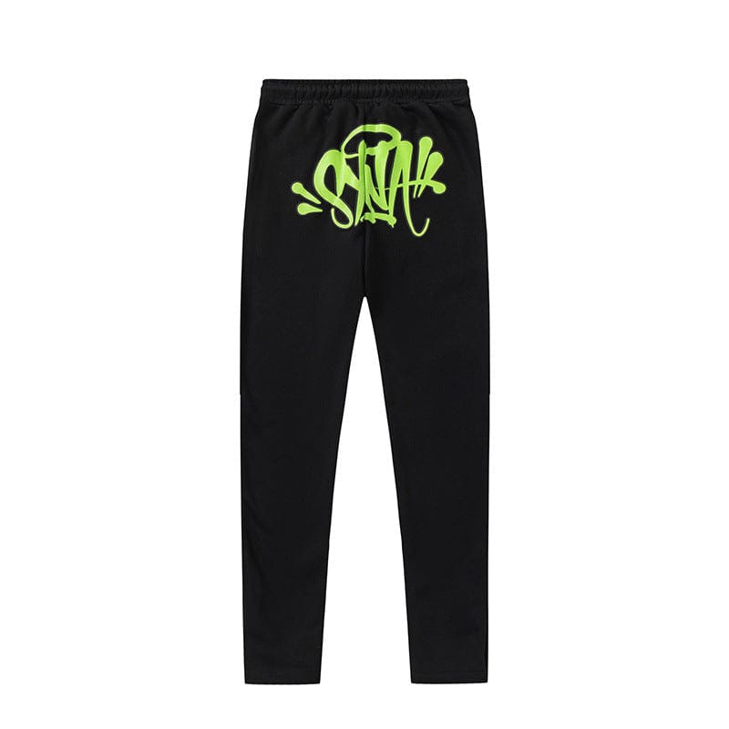 The Syna World Graphic Tracksuit Pants—black matching pants available in 4 colorways—feature neon green, graffiti-style text on the front waistband, inspired by bold graphic logo and tracksuit aesthetics.
