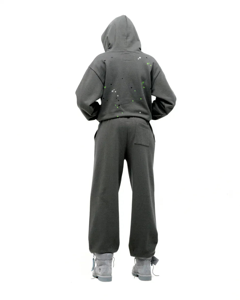Person wearing an olive green Sp5der “P!nk! Hares the Slime” 440GSM heavyweight spider-web pullover hoodie, paired with gray boots, stands with their back to the camera against a white background, embodying effortless streetwear style.