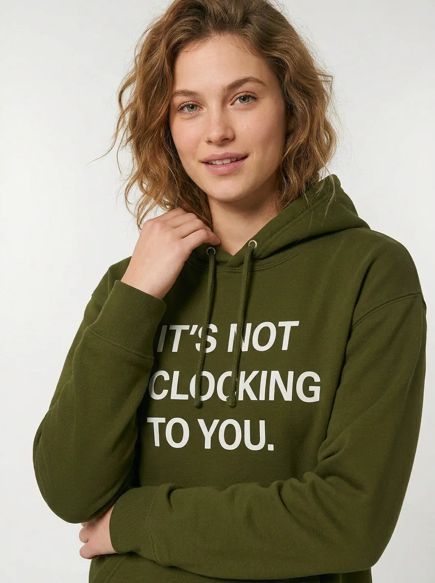 A person with wavy hair wears the Its Not Clocking To You Hoodie—a 360GSM heavyweight 100% cotton graphic pullover in olive green, featuring bold front text for standout casual style.