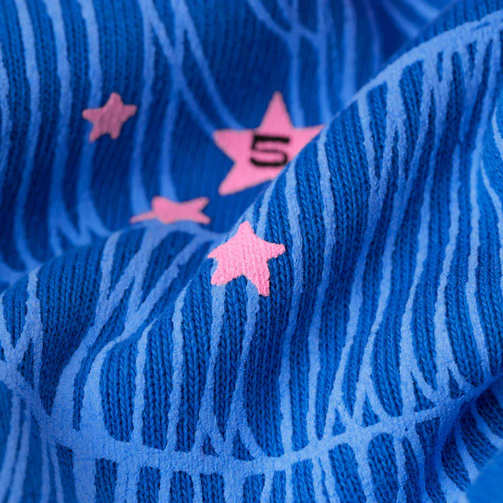 Close-up of blue heavyweight fleece with light blue wavy lines and pink stars, one marked with a 5—a bold detail featured on the Sp5der “555” Hoodie – Royal Blue 440GSM Heavyweight Spider Web Streetwear Pullover.