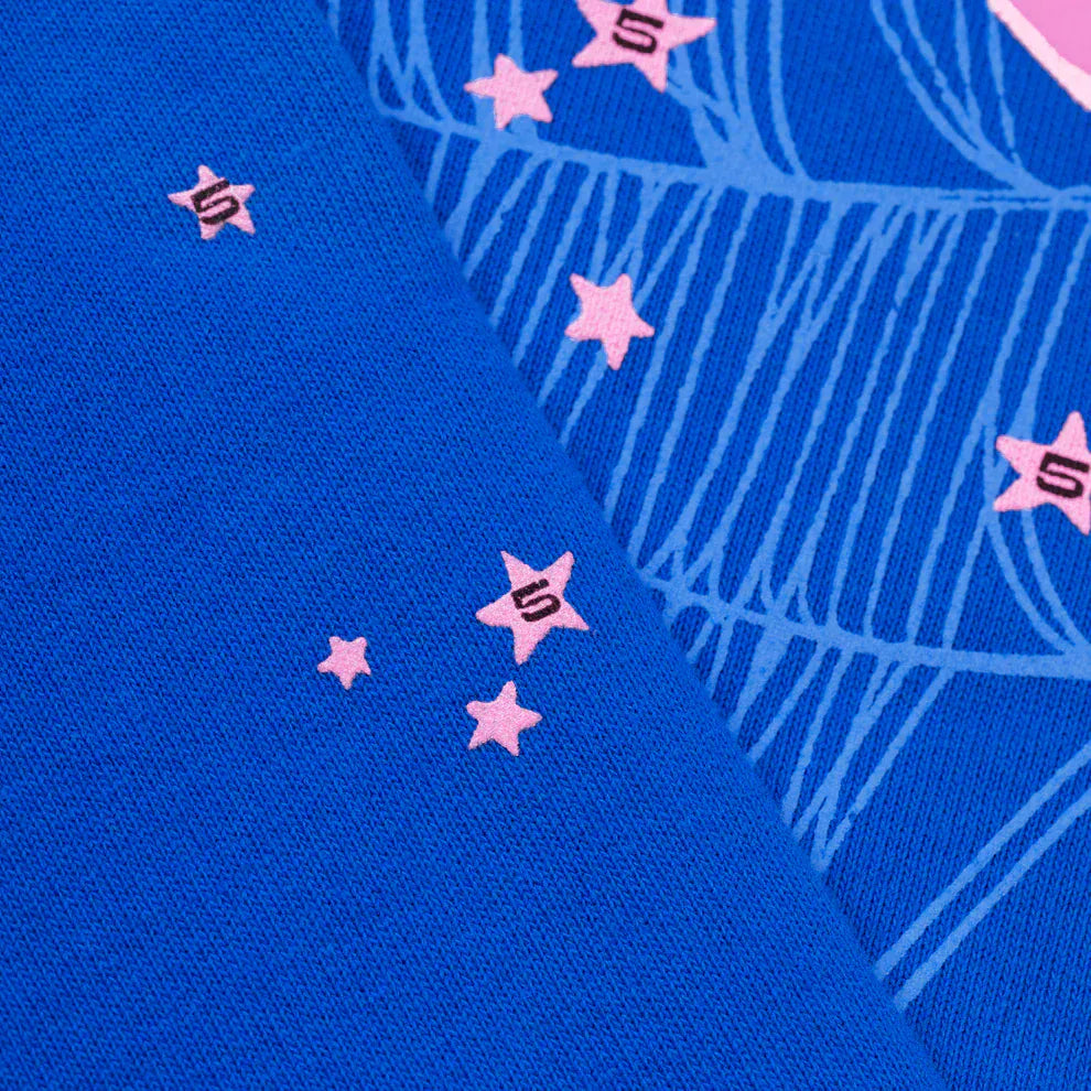 Close-up of royal blue 440GSM heavyweight cotton fleece on the Sp5der “555” Hoodie, featuring pink stars—some with the number 5—and partial light blue web details, signature to this streetwear pullover.
