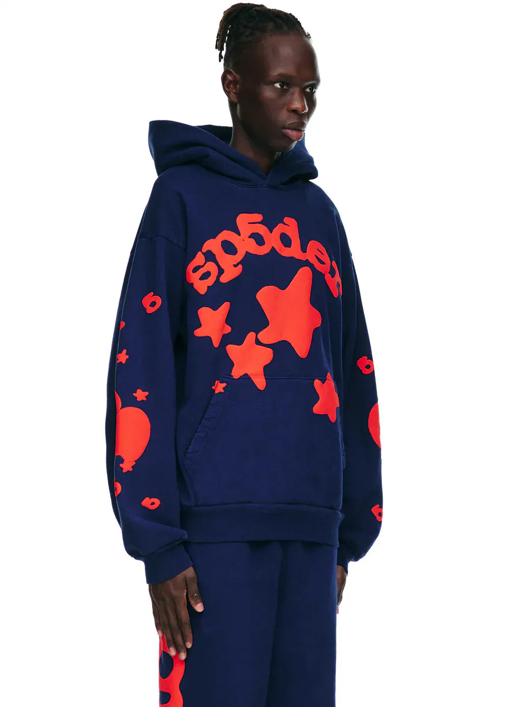 A person wears the Sp5der 440GSM Heavyweight Hoodie in navy blue with red star puff print, featuring a front pocket and hood, paired with matching pants, channeling Y2K streetwear vibes against a white background.